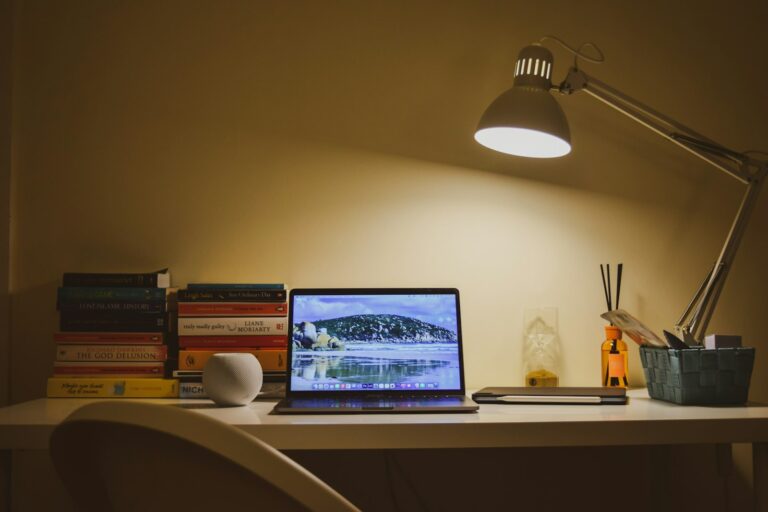 Ordinateur portable ouvert sur un bureau blanc, éclairé par une lampe, en fin de journée de travail